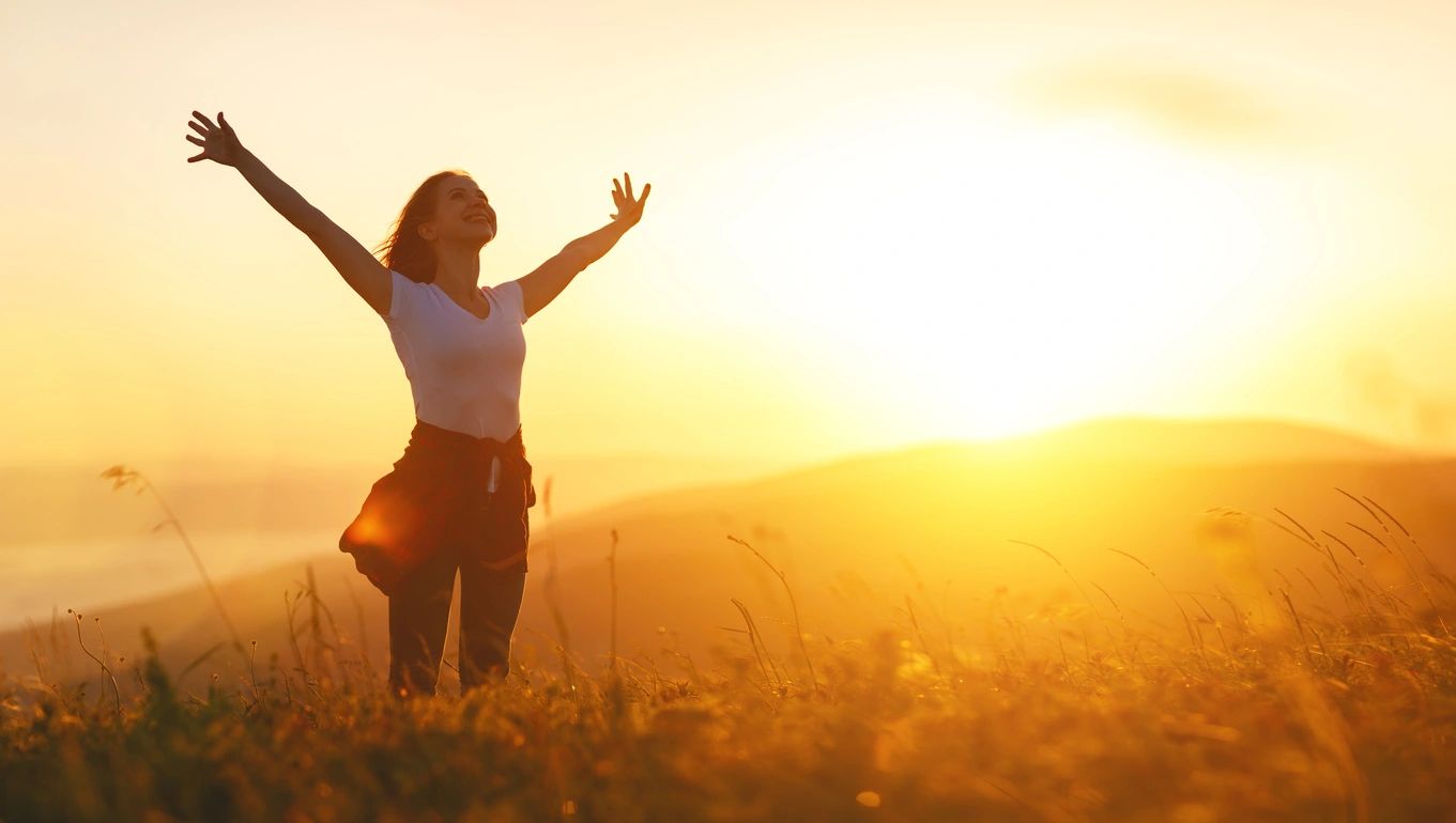Woman enjoying a sunset in a field with arms wide open.